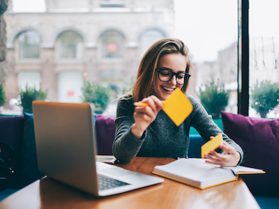 Positive hipster girl in stylish spectacles for better view using stickers for productive learning information from book, World Productivity Day